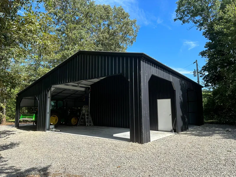 Black Pinnacle barn with a vertical roof, enclosed side rooms and a walk-in door on gravel