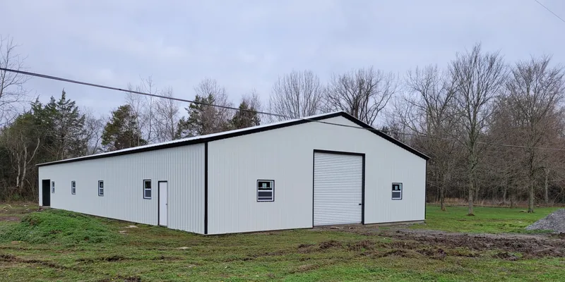 White 50 by 100 foot commercial building with a large roll-up door on open land
