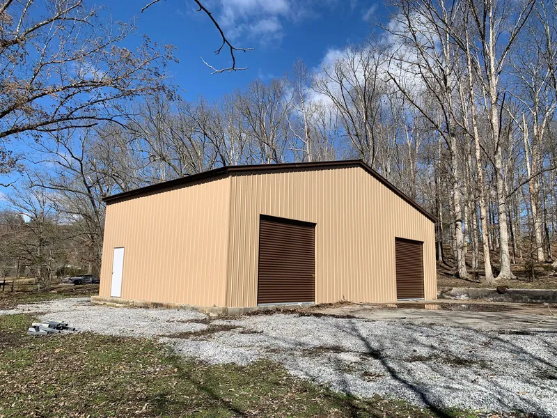 Tan garage with a brown roll-up door and walk-in door on a gravel pad